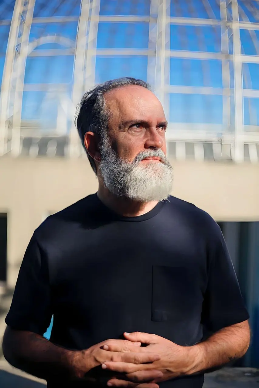 Shivanan, terapeuta holístico, em pé diante de uma estrutura arquitetônica azul e branca